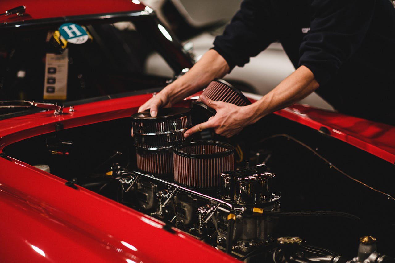 Close-up of a mechanic installing air filters on a classic red cars engine inside a garage.