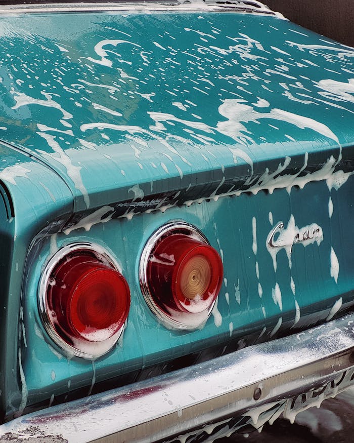 Close-up of a vintage teal car tail with soap suds during a wash, showcasing red tail lights.